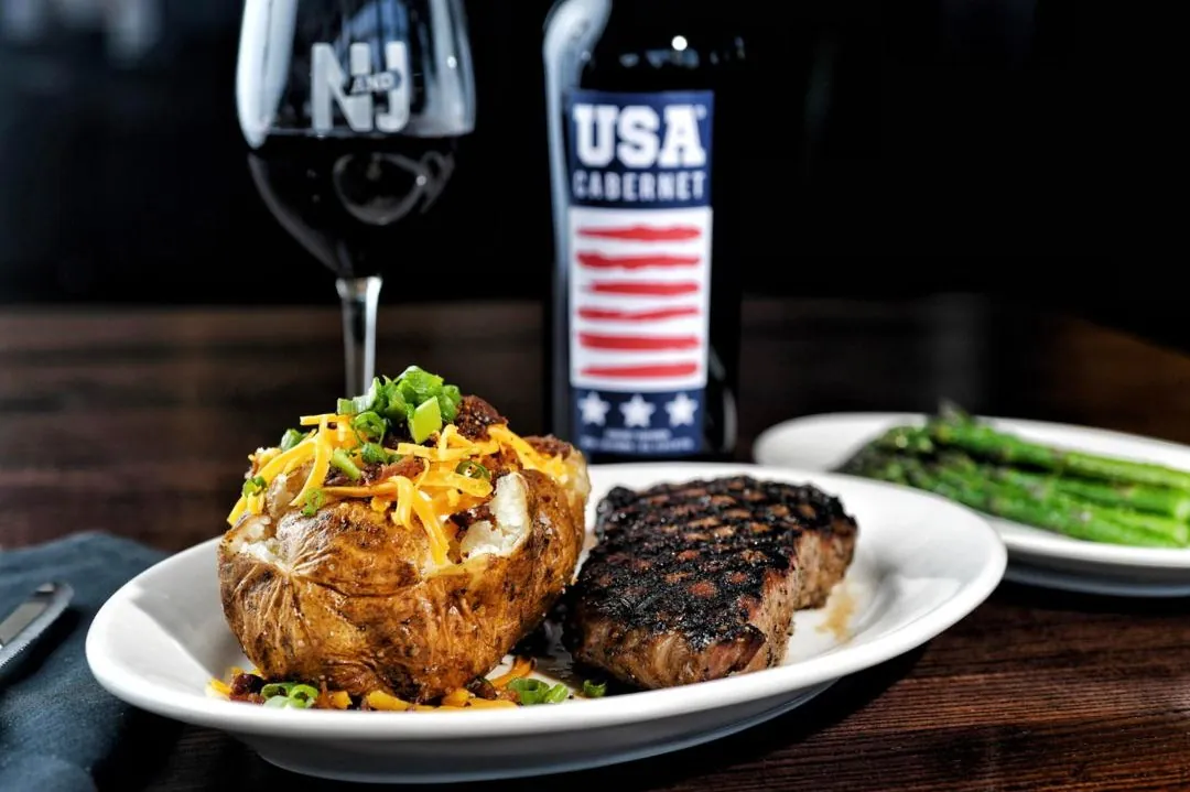 A grilled steak and loaded baked potato with a glass of red wine